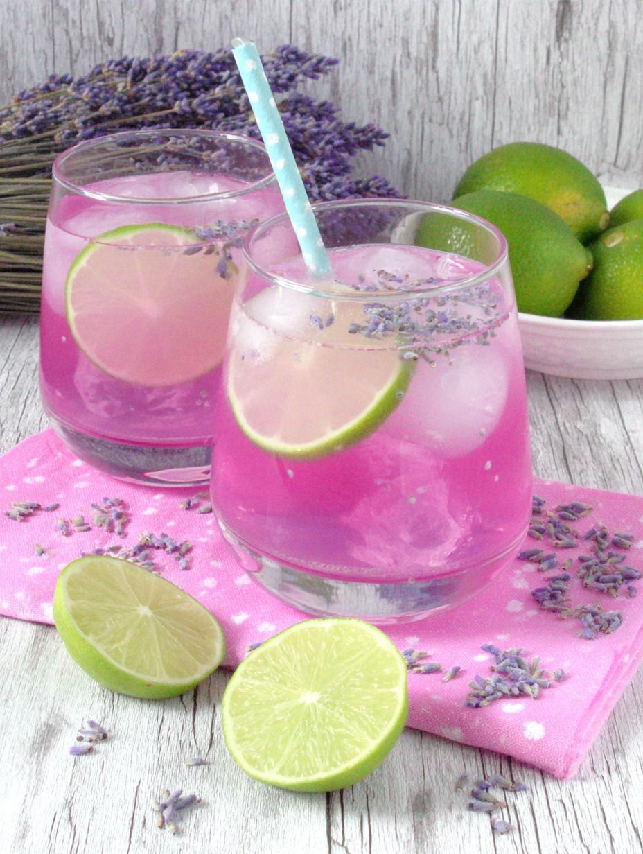 Two glasses of pink drink with limes and lavender.