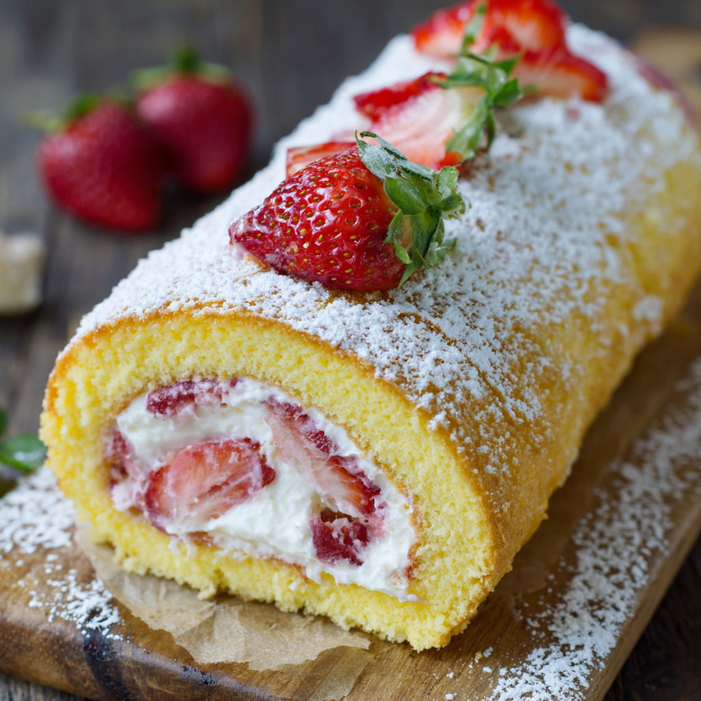 A cake roll with strawberries and cream on top.