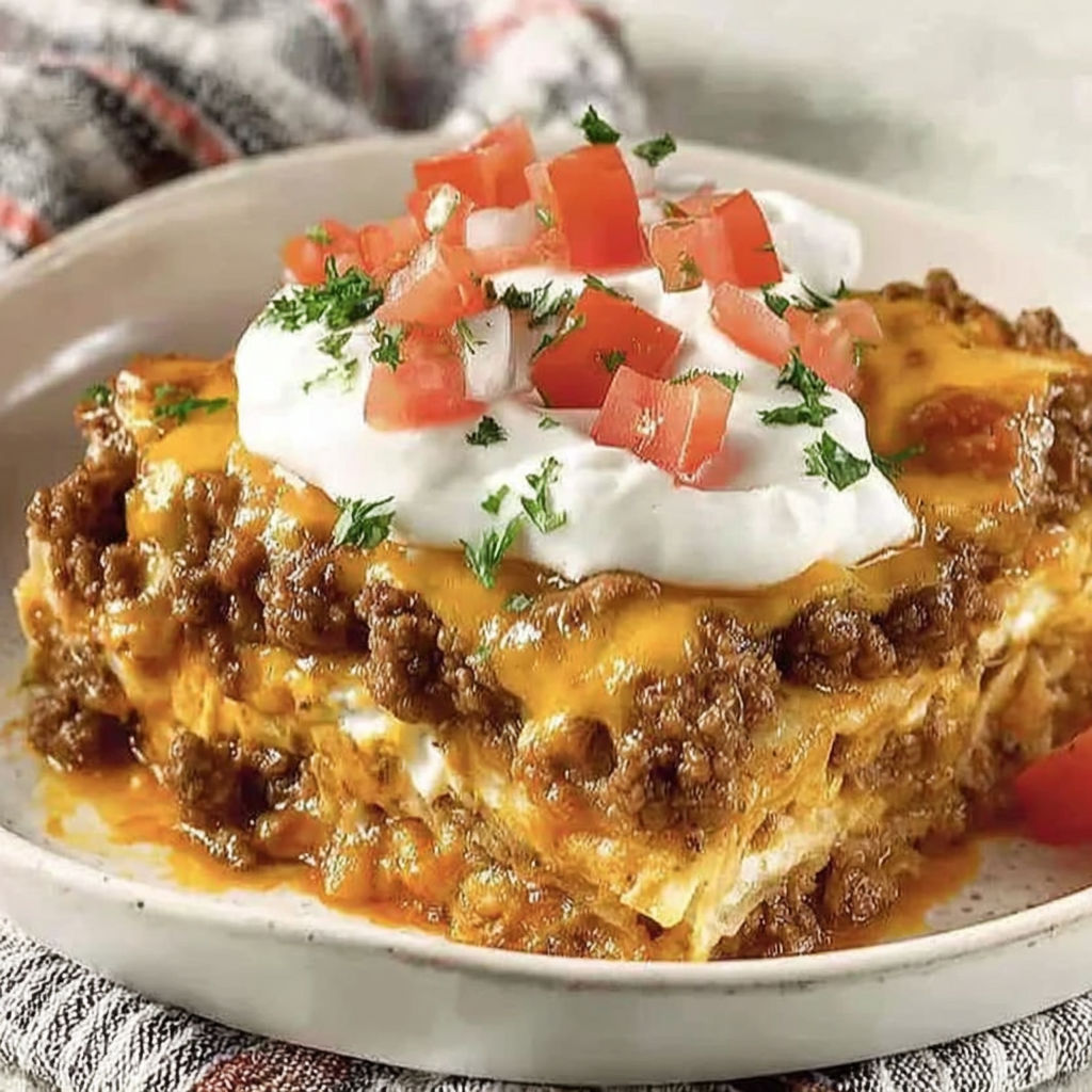 A delicious layered taco bake with tomatoes and cheese.