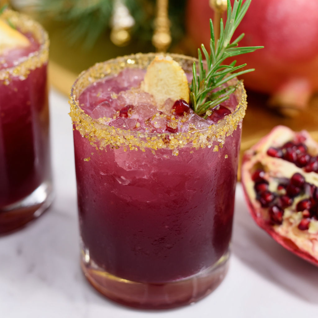 A glass of purple drink with a slice of lemon and a sprig of rosemary.