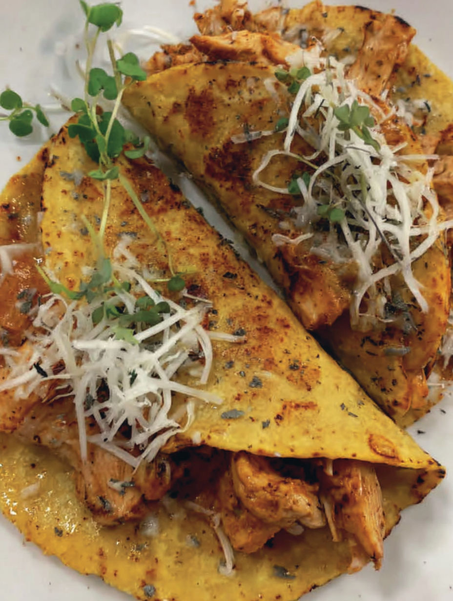 Two pieces of chicken tacos with cheese and herbs.