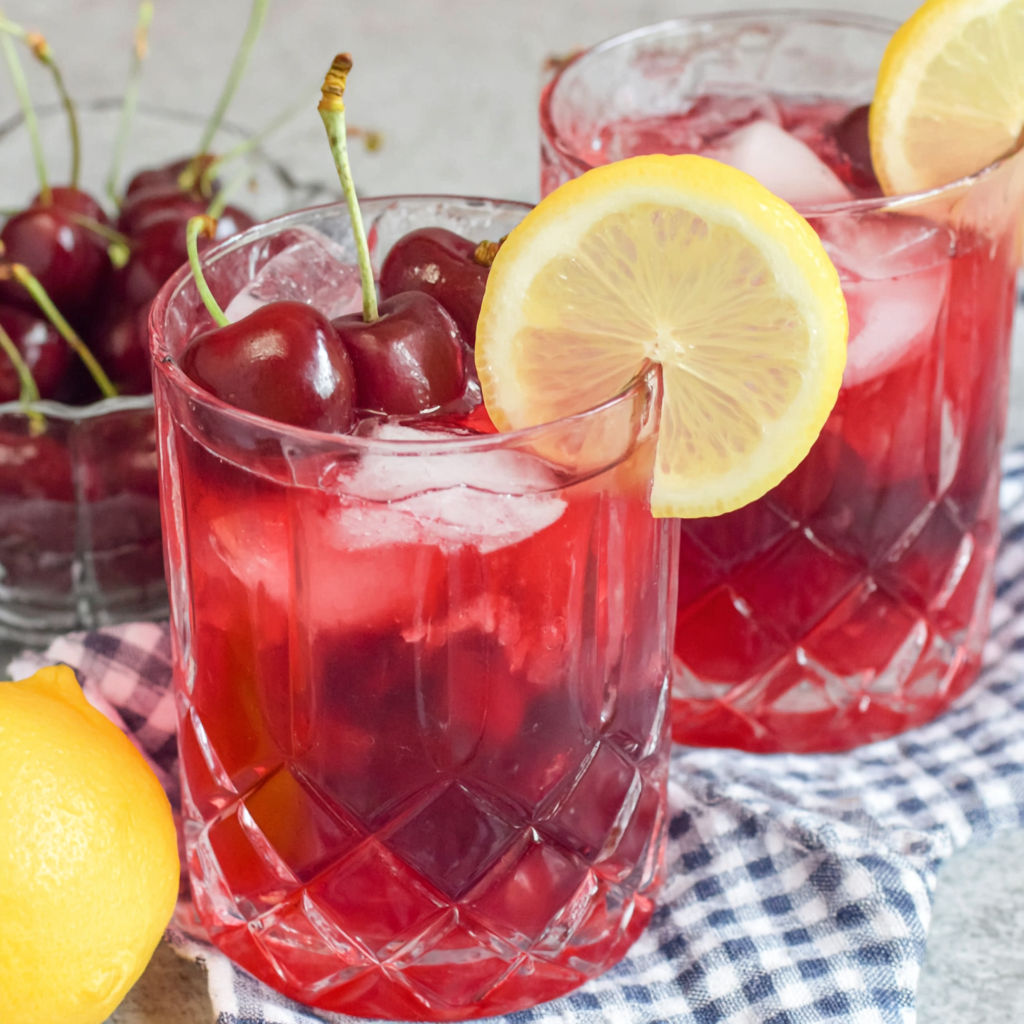 Two glasses of cherry lemonade with lemon slices in them.
