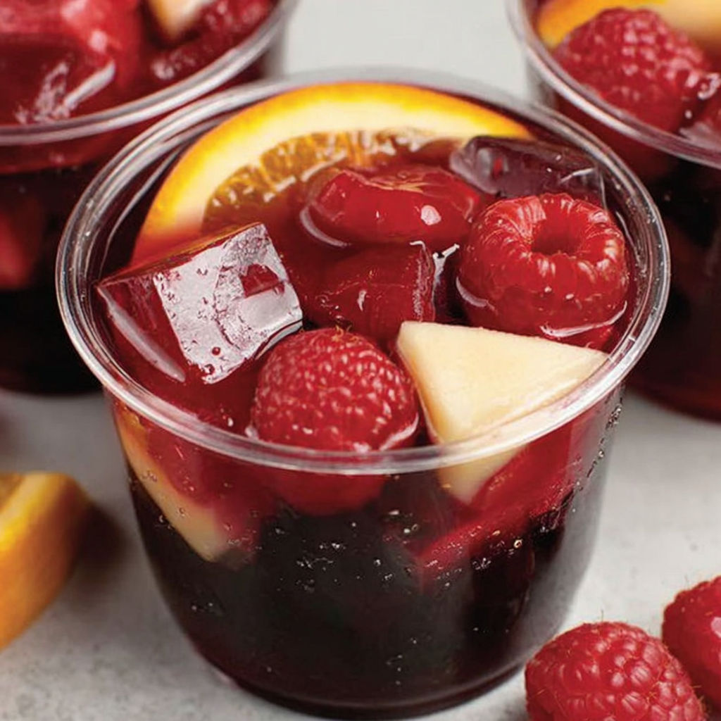 A cup of red jello shots with fruit in it.