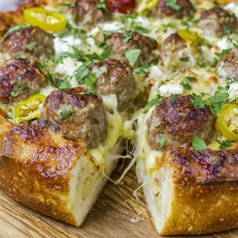 A thick slice of cheesy meatball pizza on a plate.