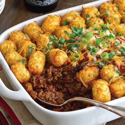 A white bowl of chili and crispy tots.