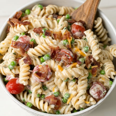 A bowl of pasta salad with bacon and peas.