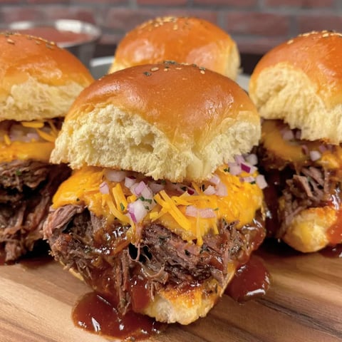 Four cheesy BBQ beef sliders on a rustic wood table.