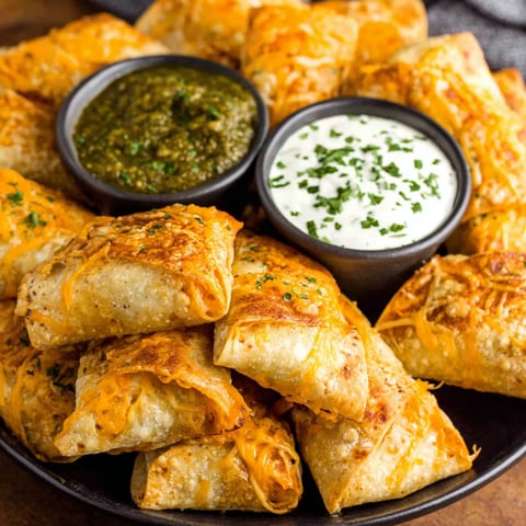 A plate of food with a bowl of sour cream and a bowl of green sauce.