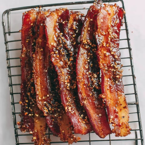 Seasoned bacon strips on a baking rack.
