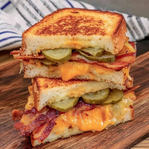 A toasted sandwich filled with melted cheese, bacon, and pickles.