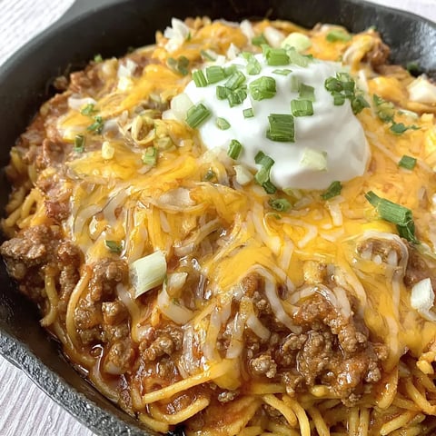 A skillet full of fideo pasta and beef, topped with sour cream.