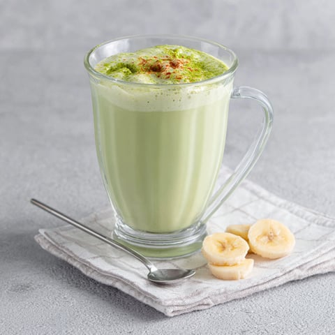 A glass of banana matcha smoothie with a spoon in it.