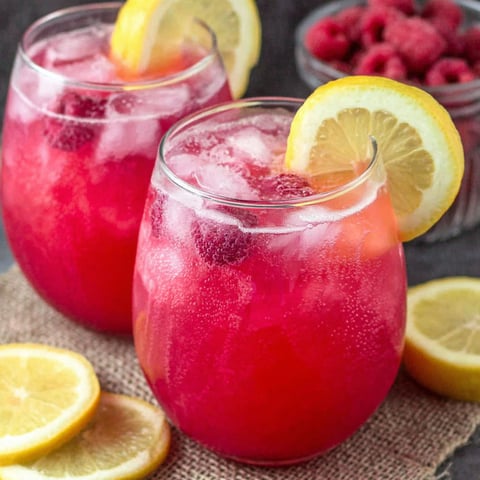 Two glasses of raspberry lemonade with slices of lemon.