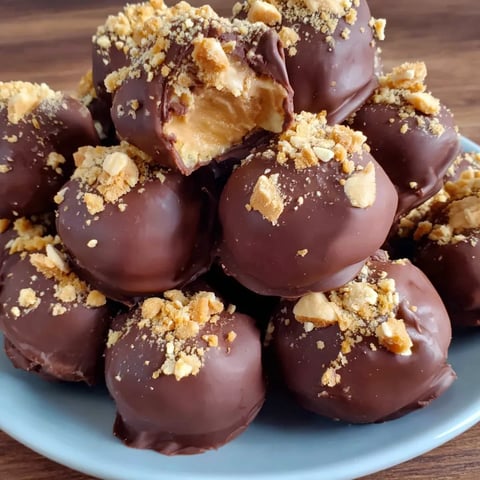A plate of chocolate balls with peanuts on top.