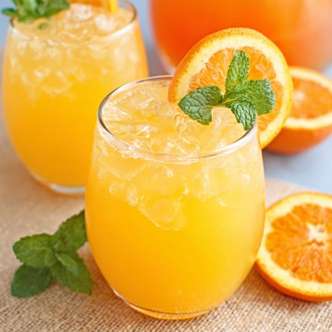 Two glasses of orange juice with slices of orange in them.