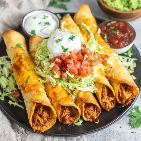 Plate of chicken flautas topped with sour cream and diced tomatoes.