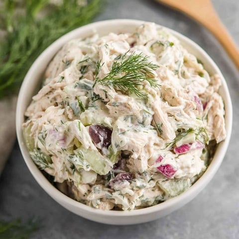 A bowl of chicken salad with a spoon in it.