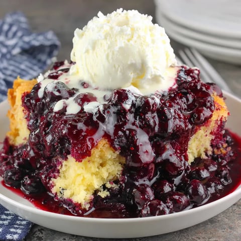 A slice of blueberry dump cake with white frosting.