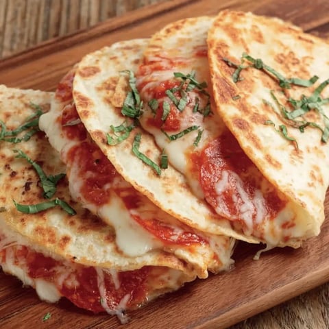 Two slices of pizza quesadilla on a wooden cutting board.