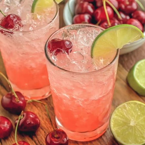 Two glasses of pink drink with cherries and limes.