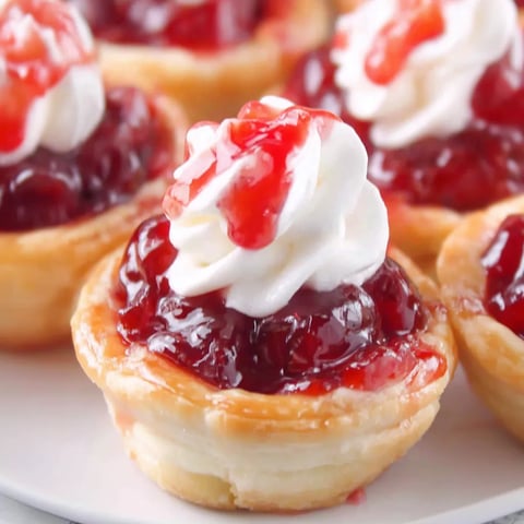 A plate of mini cherry pies with whipped cream on top.
