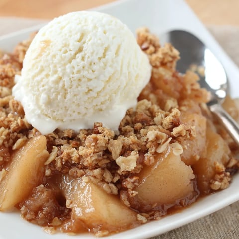 A bowl of pear crisp with a scoop of ice cream on top.