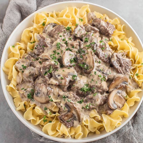 A bowl of beef stroganoff with noodles and mushrooms.
