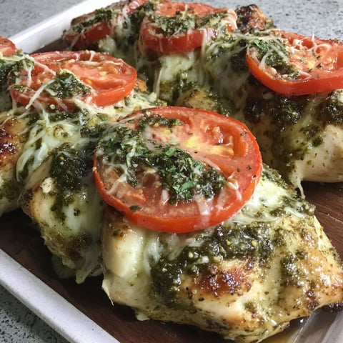 A plate of chicken with tomatoes and pesto.