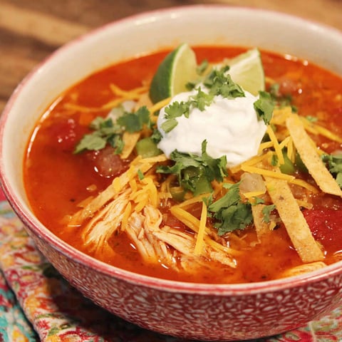 A bowl of chicken tortilla soup with a dollop of sour cream on top.