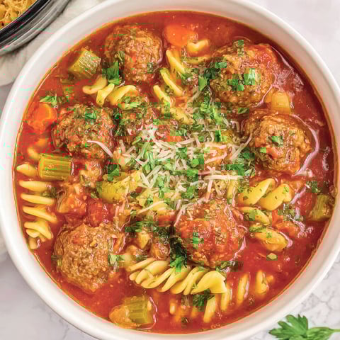 A bowl of meatball soup with noodles and vegetables.