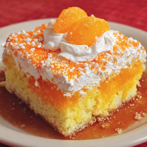 A slice of orange crush poke cake with whipped cream on top.