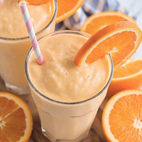 A glass of orange juice with a straw in it.