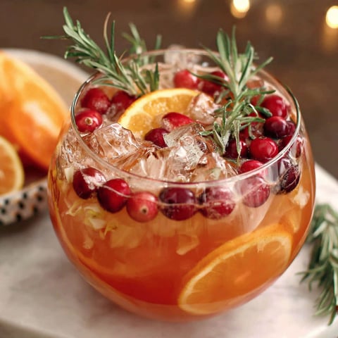A glass of non-alcoholic holiday punch with a slice of orange and a sprig of rosemary.