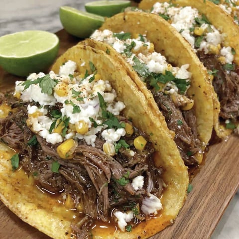 A plate of shredded beef tacos with corn and cheese.