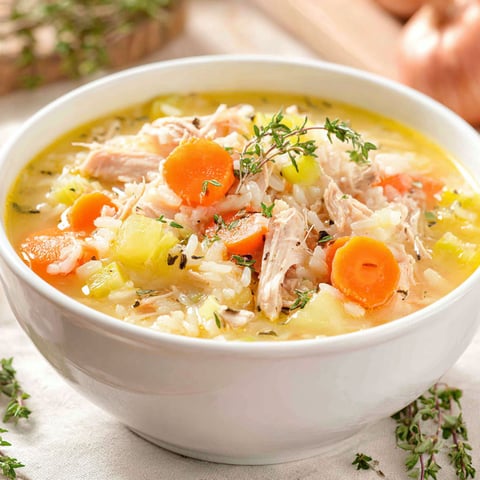 A bowl of soup with rice, carrots, and chicken.