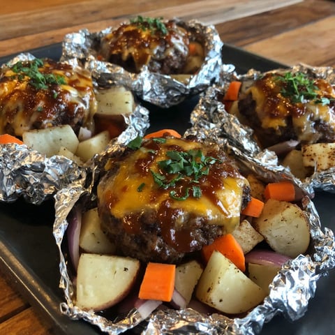Four cheeseburger foil packets with carrots and potatoes.
