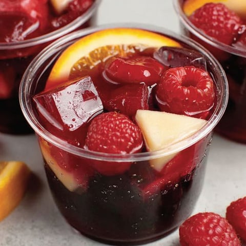 A cup of red jello shots with fruit in it.
